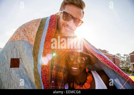 Couple wrapped in blanket smiling outdoors Stock Photo