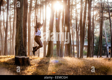 Black woman jumping from stump in sunny forest