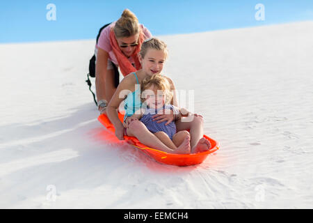 Caucasian mother and children sledding on sand dune Stock Photo