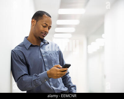 Black businessman using cell phone in office corridor Stock Photo