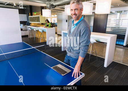 Businessman using laptop at table tennis table in office Stock Photo
