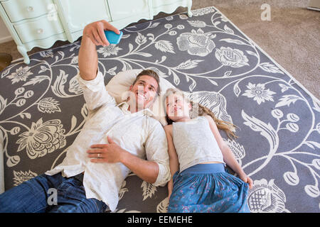 Caucasian father and daughter taking cell phone selfie on floor Stock Photo