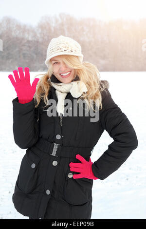 winter happy woman in snow looking up at camera and waving outside on snowing sunny cold winter day. Portrait Caucasian smiling  Stock Photo