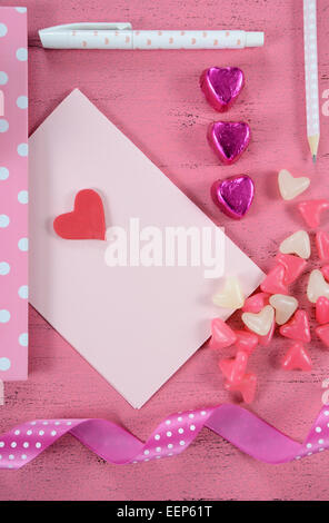 Writing love letters and cards for Happy Valentines Day with heart shape candy on pink shabby chic wood background - vertical. Stock Photo