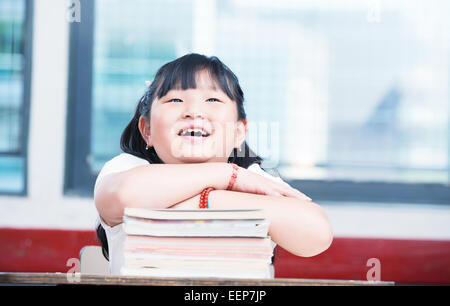 Portrait of cute asian girl on top of book stack looking upwards. School classroom happy scene. Stock Photo