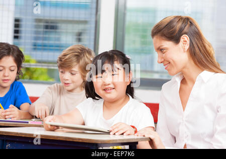 Multi-ethnic classroom. Teacher using tablet with asian student. Stock Photo