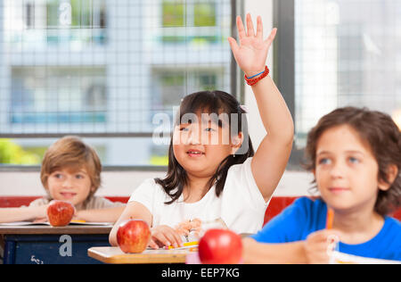 Asian girl raising hand in multi ethnic elementary classroom. Stock Photo