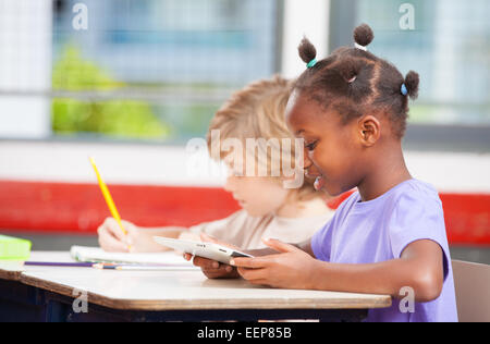 Interracial elementary classroom with students using tablet and drawing on notebook. Stock Photo