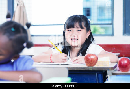 Asian girl smiling at classroom desk drawing on her book during a school lesson. Stock Photo