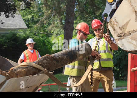 Construction workers unhooking old watermain from excavator Stock Photo