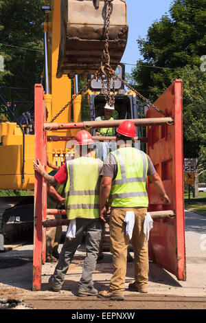 Excavator operator lifting shoring attached to bucket Stock Photo