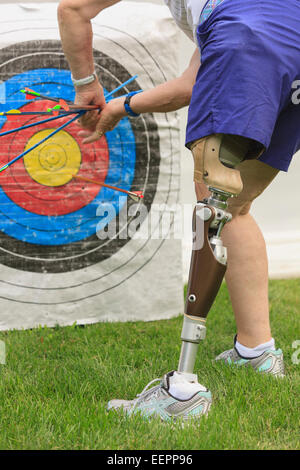 Woman with prosthetic leg pulling arrows from target after archery practice Stock Photo