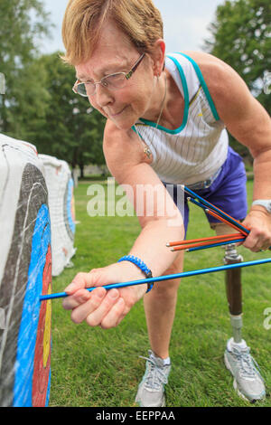 Woman with prosthetic leg pulling arrows from target after archery practice Stock Photo