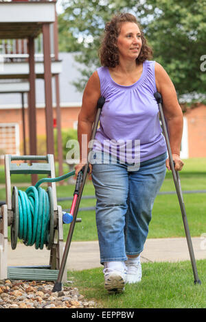 Woman with Spina Bifida walking with crutches and pulling garden hose Stock Photo