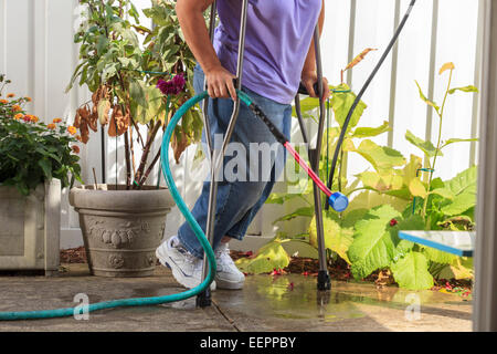 Woman with Spina Bifida walking with crutches and pulling garden hose Stock Photo