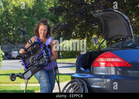 Woman with Spina Bifida taking apart wheelchair to put it in the back of car Stock Photo