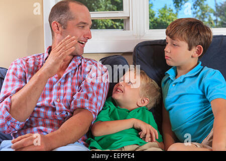 Father and sons with hearing impairments signing 'B' in American sign language on their couch Stock Photo