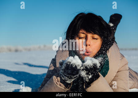 girl lying on the snow and blows snow from hands Stock Photo