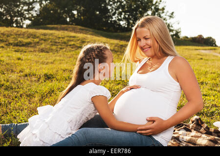 Cute little girl hugging her mother's pregnant belly. Happy sister to be is excited about meeting new baby. Mother's day concept Stock Photo