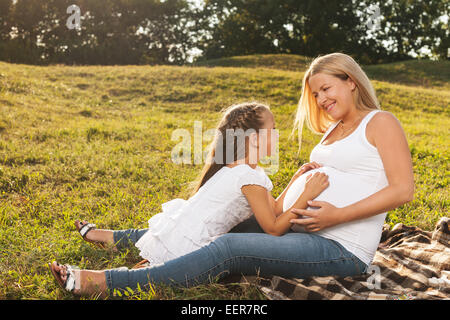 Cute little girl hugging her mother's pregnant belly. Happy sister to be is excited about meeting new baby. Mother's day concept Stock Photo