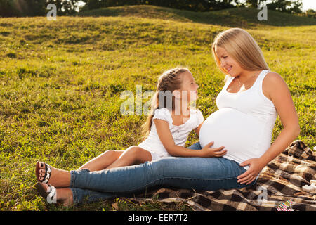 Cute little girl hugging her mother's pregnant belly. Happy sister to be is excited about meeting new baby. Mother's day concept Stock Photo