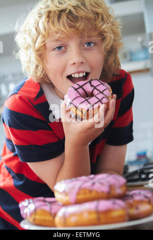 Boy Eating Iced Donut In Kitchen Stock Photo