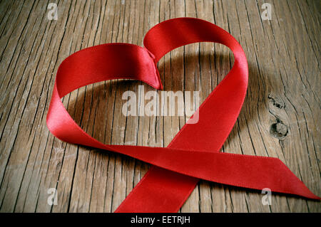 a red satin ribbon forming a heart on a rustic wooden surface Stock Photo