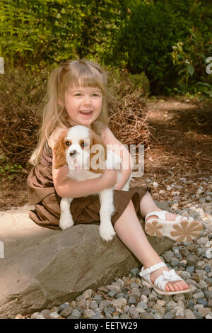 Three year old girl holding a  female Cavalier King Charles Spaniel, Mandy, a 15 week old puppy, in western Washington, USA Stock Photo