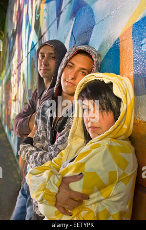Three teenagers leaning against a graffiti covered wall Stock Photo