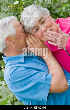 Senior man whispering into ear of wife Stock Photo