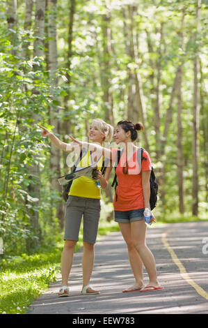 Two girl friends standing on a bike path in the forest pointing Stock Photo