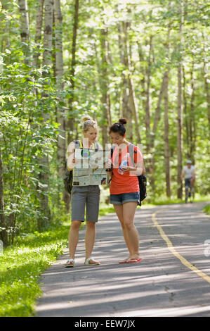 Two girl friends standing on a bike path in the forest and holding a map Stock Photo