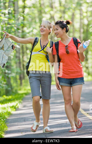 Two girl friends walking on a bike path in the forest with a map Stock Photo