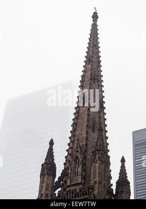 The Spire of Trinity Church in Lower Manhattan: a study in contrasts. The dark stone spire of Trinity topped with a gold cross Stock Photo