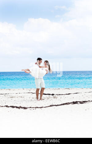Happy newlyweds in white dresses having fun on beach with turquoise sea background Stock Photo