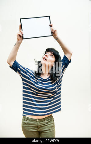 Pretty brunette girl looking and showing blank picture frame up on her head on white background Stock Photo