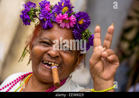 Elderly Cuban woman with flower headdress and cigar, making peace sign, Havana, Cuba Stock Photo