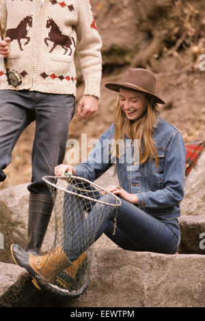 Young couple in a forest, fishing in a river, smiling woman holding a fish in a net. Stock Photo