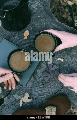 Couple having coffee in a forest, two mugs of coffee, a coffee pot and a pair of gloves on a tree trunk. Stock Photo