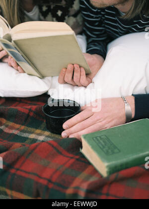 Close up of young man reading a book, holding a mug.