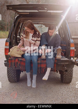 Young couple sitting in the back of their car, putting on boots. Stock Photo