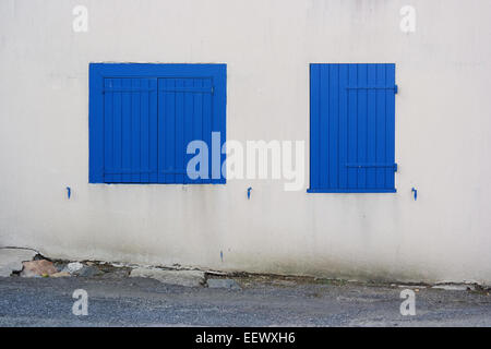 Two dissimilar windows clossed by blue shutters on a white wall Stock Photo