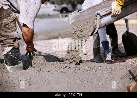Closeup of Masons working quickly to place and finish fresh concrete as it hardens on a sunny day Stock Photo