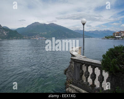 View across Lake Como to the surrounding snow capped mountains from the balustraded promenade of Bellagio in Italy with a ferry crossing the lake Stock Photo