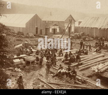 Resting, Dawson City - bird's-eye view of men sitting on logs and standing in construction area with view of the 'Eldorado Restaurant' and the 'Miners Home' in the background. Stock Photo