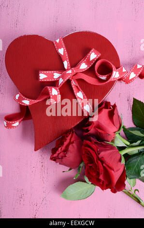 Happy Valentines Day red heart shape gift box with red roses on shabby chic vintage style pink wood table background, vertical. Stock Photo