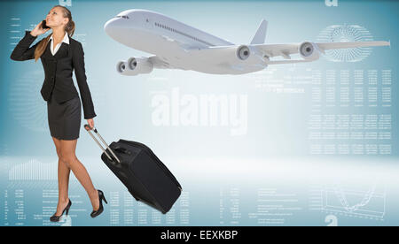 Businesswoman carrying suitcase while talking on the phone. Image of flying airliner beside Stock Photo