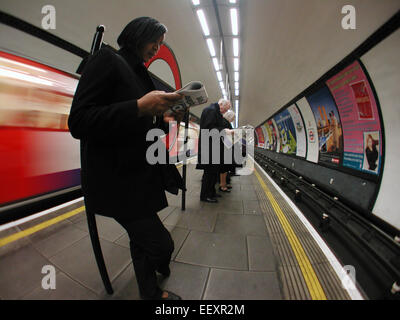 Commuters reading daily newspapers waiting on the platform for a Tube train during the morning rush hour at Clapham Common Underground station, London, UK. Stock Photo
