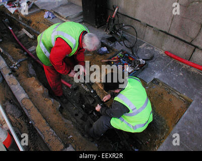 Telecommunication fitters and cable layers in fluorescent jackets working on underground telecom cables beneath the street near Southwark Bridge, London, UK Stock Photo