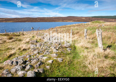 Bronze age ring cairn beside Llyn Brenig in North Wales with a fishing boat on the water of the reservoir. Stock Photo